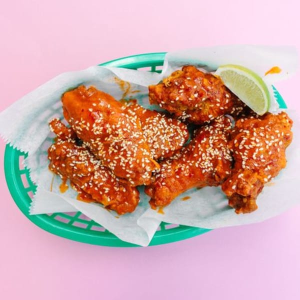 Yumbii's Mexican-style chicken wings, coated in a spicy sauce and sesame seeds, with a lime wedge.