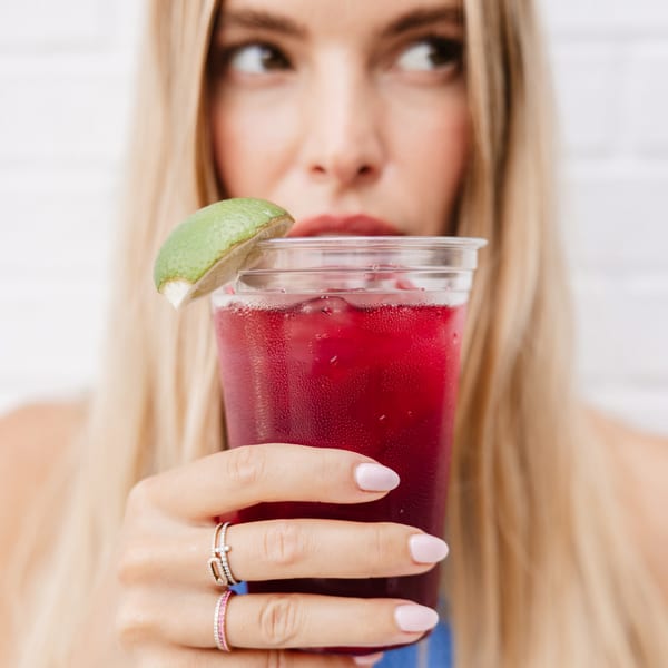 Blonde woman holding a Yumbii red drink with a lime wedge, looking away.