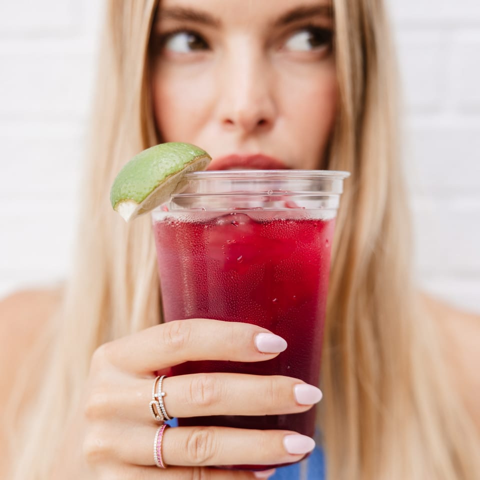 Blonde woman holding a Yumbii red drink with a lime wedge, looking away.