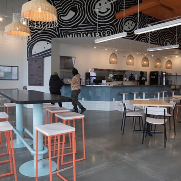 Modern Yumbii restaurant interior with high tables, orange stools, and a black and white mural.