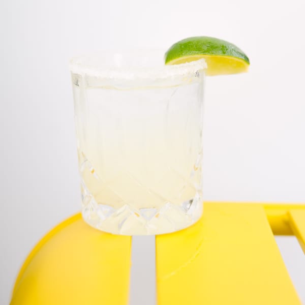 A Yumbii margarita in a salt-rimmed glass with a lime wedge, on a bright yellow surface.