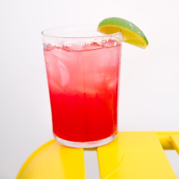 A vibrant red Yumbii margarita with a salted rim and lime wedge, on a yellow surface.