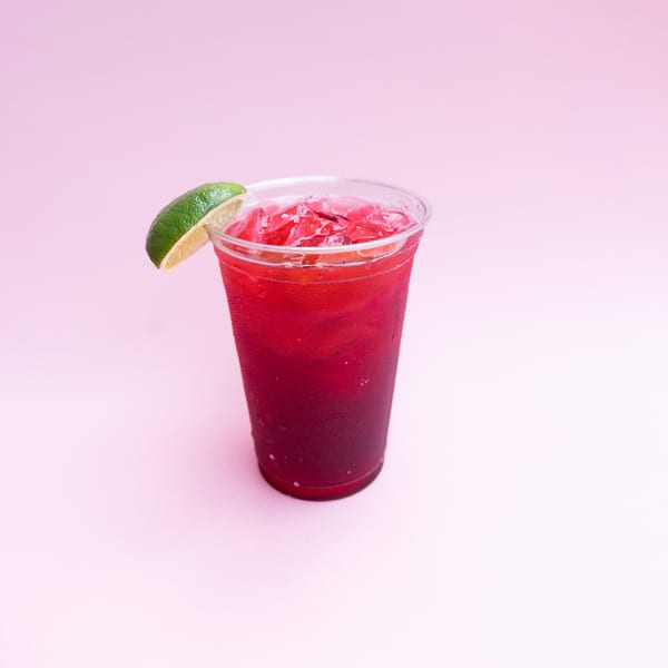 Yumbii's vibrant red Mexican drink with ice and a lime wedge, in a clear plastic cup.