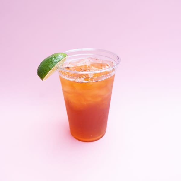 Iced tea with a lime wedge in a clear plastic cup on a pink background.