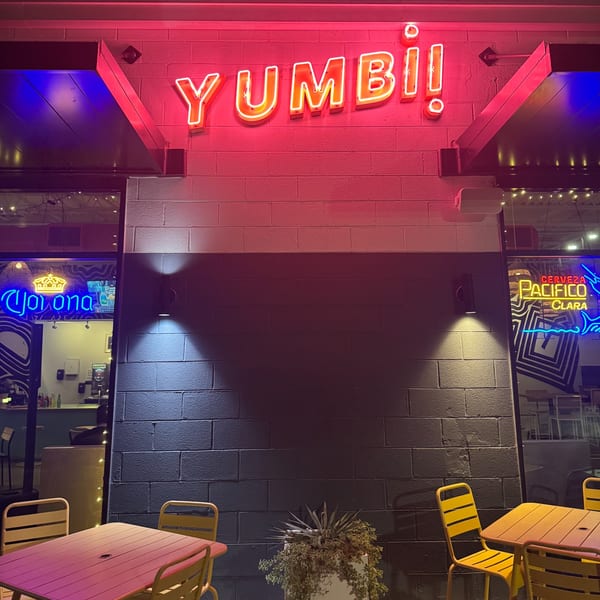 The Yumbii restaurant exterior at night, with a bright red neon sign and outdoor seating.