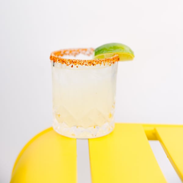 Yumbii's margarita with a chili-lime rim and lime wedge, on a bright yellow table.
