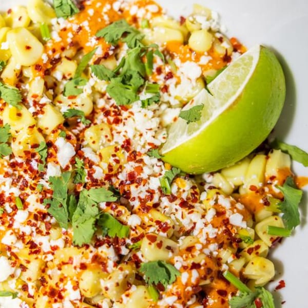 Yumbii's Mexican street corn with cotija cheese, chili flakes, cilantro, and a lime wedge.