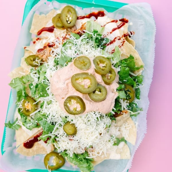 Yumbii's loaded nachos with shredded cheese, lettuce, jalapeños, and a creamy sauce in a green basket.