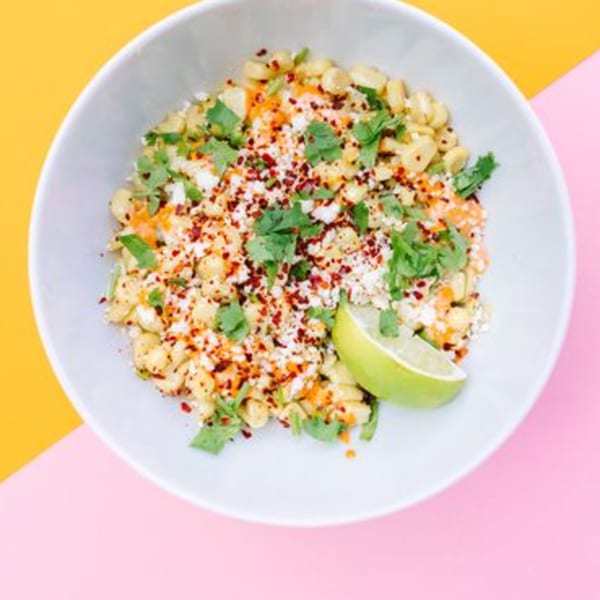 Yumbii's Mexican street corn in a white bowl, topped with cheese, chili flakes, cilantro, and lime.