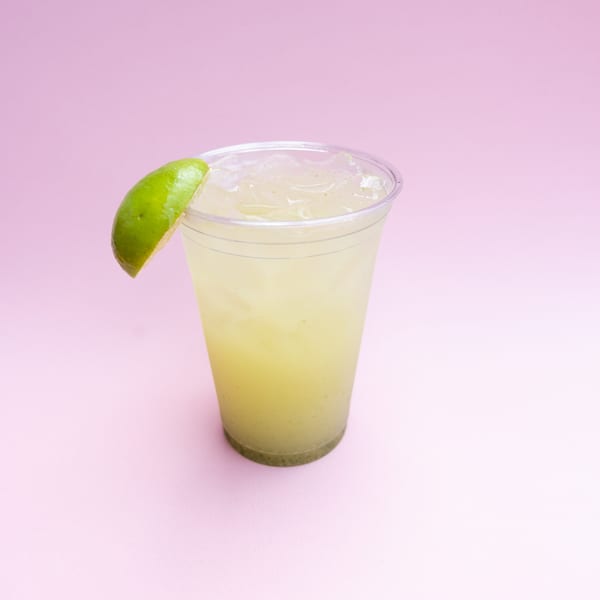 Yumbii's Mexican limeade with ice and a lime wedge in a clear plastic cup.