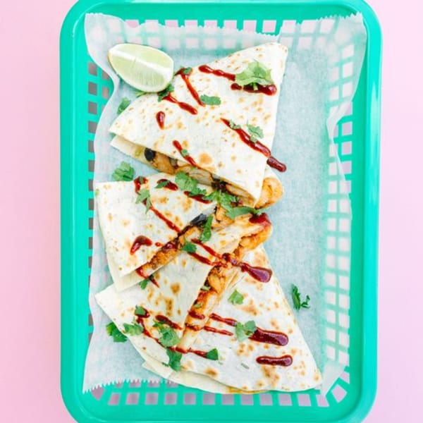 Yumbii's chicken quesadillas with sauce and cilantro, served in a green basket with a lime wedge.