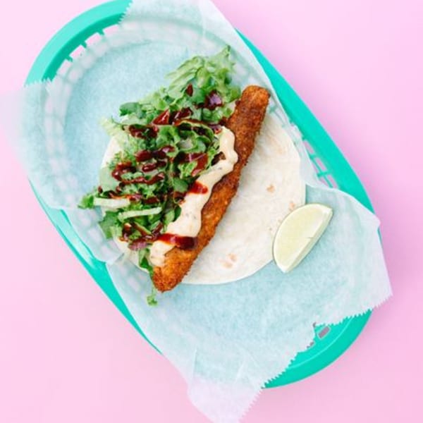 A Yumbii fish taco with lettuce, sauce, and a lime wedge in a green basket.